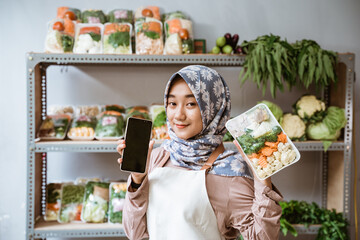Woman greengrocer showing vegetables and showing a phone screen