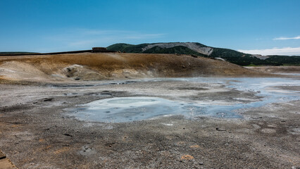 The water in the thermal springs is blue and opaque. Sulfur deposits are visible on the surrounding soil. A mountain range against an azure sky. Kamchatka. The caldera of the extinct volcano Uzon
