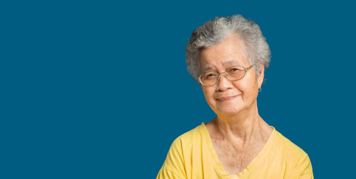 Elderly Asian Woman Looking At The Camera With A Smile While Standing On A Blue Background