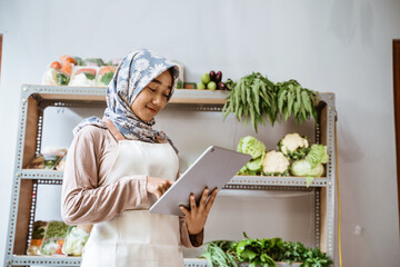 Girl in headscarf selling vegetables using a pad
