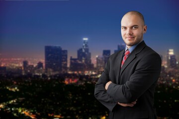 Fototapeta na wymiar Smiling young businessman with arms crossed in city background
