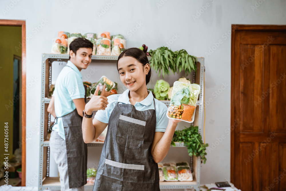 Wall mural Vegetable selling girl with thumbs up with a male partner