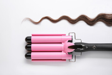 Modern triple curling iron and brown hair lock on white background, top view