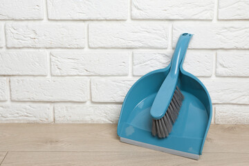 Plastic whisk broom with dustpan near white brick wall indoors. Space for text