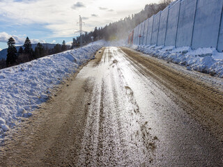 Winter road in the mountains, traveling through snowy mountainous terrain on a sunny frosty day.