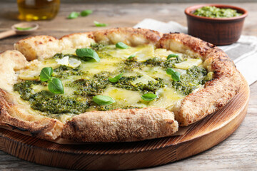 Delicious pizza with pesto, cheese and basil on wooden table, closeup