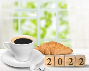 Wooden cubes with number 2022 on a table with coffee, croissant