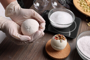 Woman holding handmade bath bomb above wooden table, closeup