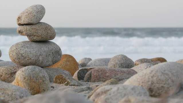 Rock balancing on pebble beach, Monterey 17-mile drive, California coast, USA. Stable pyramid stacks of round stones, sea ocean water waves crashing at sunset. Serenity harmony, calm zen meditation.