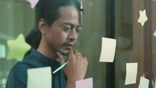 Businessman sticking adhesive notes on glass wall in creative in office, The man working write work with stickers reminder on paper on whidows
