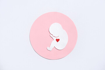 Paper silhouette of a human embryo with a red heart on a white background. Flat lay, place for text.