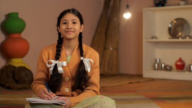 A young schoolgirl of an Indian village studying alone under an electric bulb - Beti Bachao Beti Padhao  girl education  girl portrait . A sweet girl with braided hair completing school homework - ...