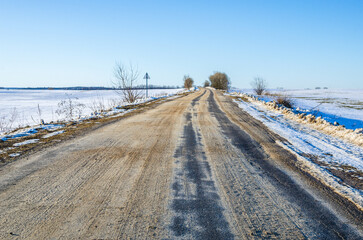 Winter road covered with sand. Asphalt road going into the distance in winter