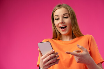 Naklejka premium Excited surprised young woman using mobile phone against studio background