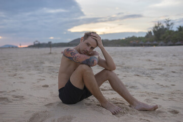 Full-length portrait of handsome caucasian man sitting on the sand on the beach