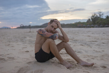 Fototapeta na wymiar Full-length portrait of handsome caucasian man sitting on the sand on the beach