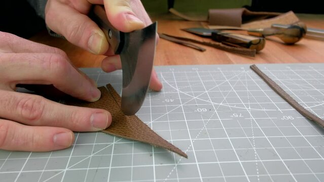 Close up hands tanner cuts special halberd cutting knife leather piece in workshop. Craft production.
