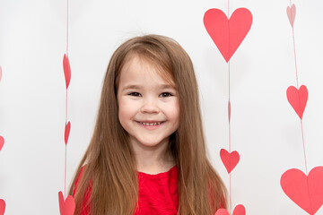 Portrait of a girls child with long flowing hair in red clothes on a white background with hearts. Concept Valentines Day.