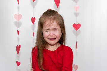 Tears and sadness on Valentines Day. A little girl cries on a white background with hearts.