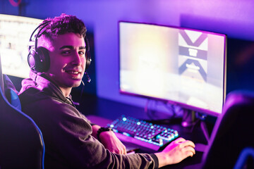 A happy gamer in gaming room playing video games and smiling at the camera. - obrazy, fototapety, plakaty