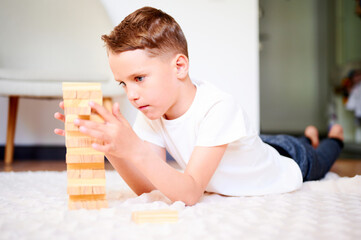 Boy playing wooden block removal tower game at home. Board game Jenga. Kids leisure concept.