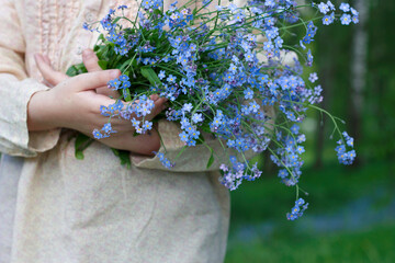 girl holding bouquet of forget me not blue flowers in spring forest