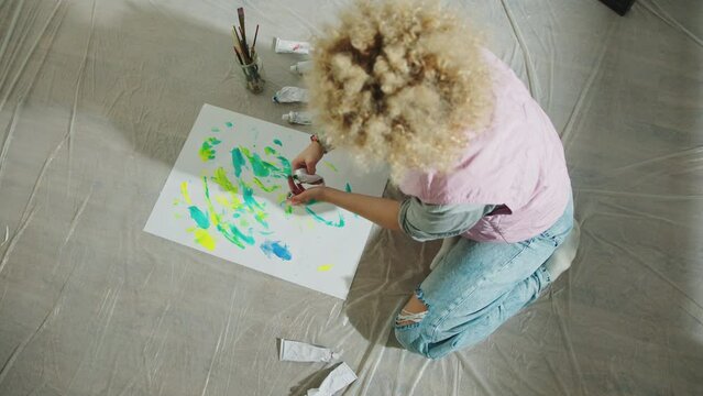 Artist girl shot from above, sitting on the floor using the colors on the sheet