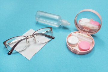 Glasses, contact lens kit and solution on a blue background. Choosing between glasses and lenses....