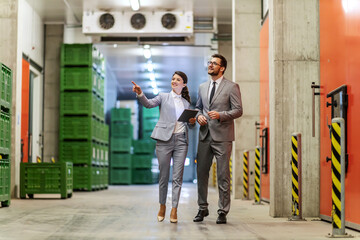 A businesspeople walking through warehouse with tablet and checking on logistic.