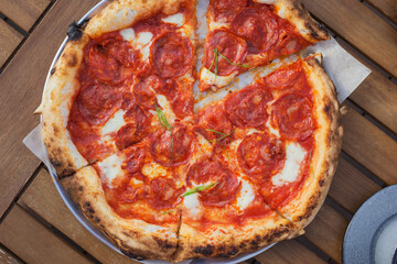 Top view on pizza with chorizo - spicy pork sausage, stracciatella, tomato sauce, green onion on wooden table. Lifestyle background.