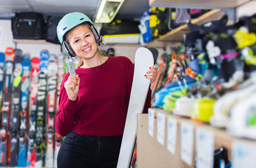 positive european woman in helmet is demonstraiting ski in shop..