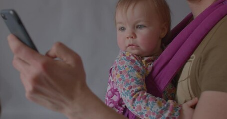 Happy little baby smiling, cuddling up to parent, looking at camera, pointing finger at phone in hands of busy father. Technology has transformed the way parents interact with their children.