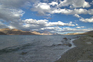 A view of lake Pangong Tso surrounded by the Himalayas and cloudy sky.