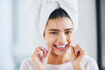 Oral hygiene is vital. Portrait of a beautiful young woman flossing her teeth in the bathroom at...
