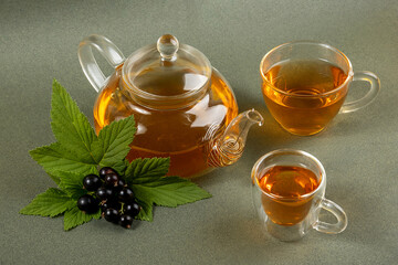 Black currant tea. Transparent glass teapot, cups of tea and black currant berries on a green...