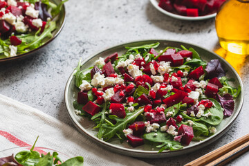 Arugula, Beet and cheese salad with pomegranate and dressing on plate on grey stone kitchen table background, place for text, top view