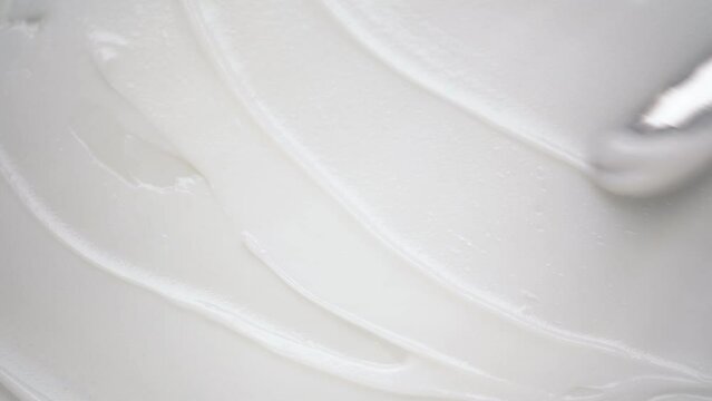 Applying soft moisturizing lotion over white background using shiny metal spatula upper macro view. Antiaging skincare product