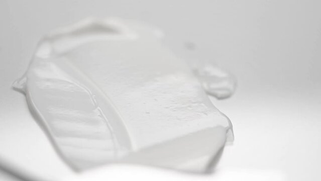 Spreading soft cream over white background with small metal spatula macro view. Texture of natural skincare cosmetic product