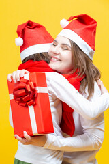 Holidays Concepts. Mother and Her Female Kid In Santa Hats While Embracing With Each Other And Having Big Wrapped Christmas Present Behind Back While Cuddling To One Another.
