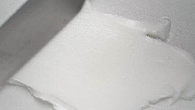 Spreading antiaging squeezed cream jet with spatula over white background upper macro view. Professional cosmetic product for beauty