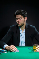 Nervous and Concentrated Handsome Caucasian Brunet Young Pocker Player At Pocker Table With Chips While Drinking Alcohol While Playing.