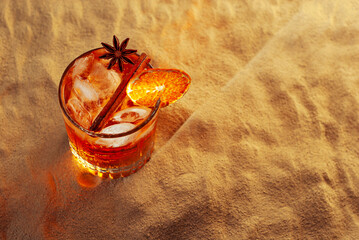 Orange cocktail on yellow sand. Alcoholic drink with ice, orange and cinnamon close up. Copy space...