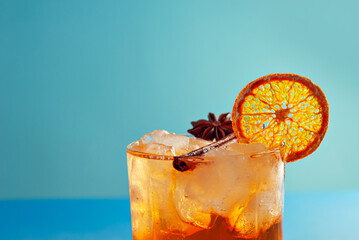Orange cocktail on a blue background. Alcoholic drink with ice, orange and cinnamon close up.