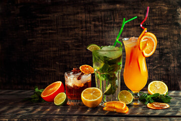 Cocktails with straws, ice and fruits on a black background. Alcoholic drinks on an old wooden table close up. Drink on a shabby brown board. Copy space and free space for text near the glass.