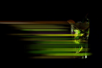 Cocktail with straws, ice and fruits on a black background. Mojito on an old wooden table close up. Copy space and free space for text near the glass. Motion blur as an artistic effect.