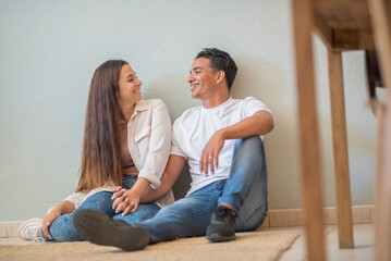 Mortgage and loan banking economy with young couple of buyers sitting on the floor at home and smile planning to furnishing. Cheerful happy people in love and relationship. Interracial boy and girl
