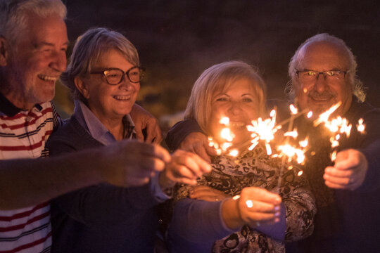 Group of senior people celebrate together in friendship with sparkler fire light by night. New year eve and party event nightlife concept lifestyle witn mature men and women having fun