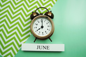 June and alarm clock on green background