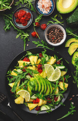 Vegan vegetarian salad with pineapple, arugula, avocado and dried cherry on black plate on dark stone kitchen table, top view. Healthy eating, clean diet food, weight loss concept