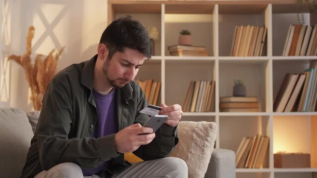 Blocked credit card. Payment problem. Declined transaction. Frustrated man typing CVV code on phone annoyed with verification security at home copy space.